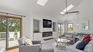A modern living room with a flat-screen TV, grey sofas, a coffee table, and a ceiling fan. - Sea La Vie: Oceanside, Hot Tub, Shared Pool (Corolla)