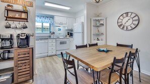 A modern kitchen with white cabinets, a wooden dining table, and a clock on the wall. - Gorgeous 2 Bedroom Condo - Pool/Tiki Bar/Beach (Hilton Head Island)