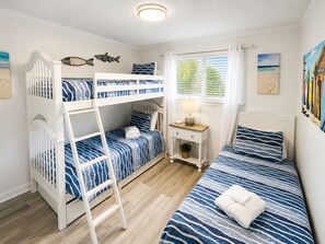 Una habitación con literas, una mesita de noche con lámpara y una ventana con cortinas.