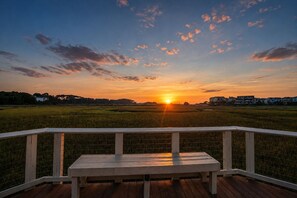 Una terraza de madera con un banco que da a un atardecer sobre un campo con casas a lo lejos.