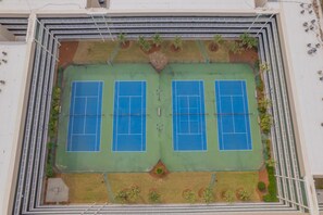 Vue aérienne d’un complexe de courts de tennis comprenant plusieurs terrains, entouré de verdure et délimité par une clôture blanche.