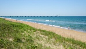 Une plage avec une longue jetée qui s’avance dans la mer, un rivage sablonneux et des dunes herbeuses.