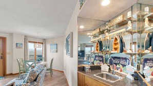 Een gezellige woonkamer met een bank, een eettafel en stoelen. Er is een keuken met een spoelbak en een bordje met de tekst 'Welkom in ons Strandhuis'.