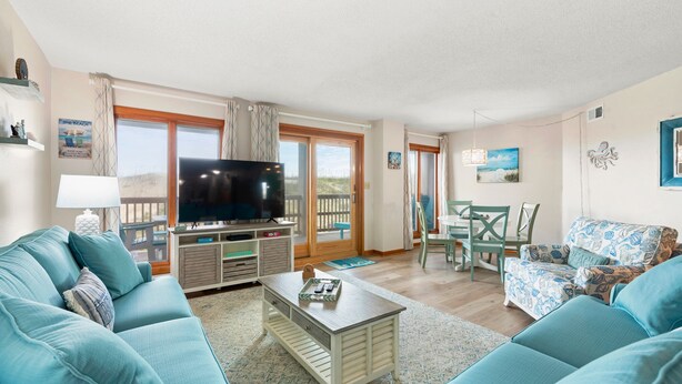 Een woonkamer met een televisie, bank, salontafel en een balkon met tafel en stoelen.