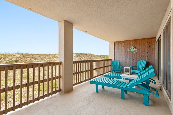 A balcony with a wooden railing, a wooden wall with a decorative octopus, and two turquoise lounge chairs.