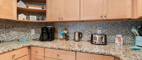 Una cocina con armarios de madera, salpicadero de azulejos y diversos electrodomésticos, incluyendo cafetera, hervidor y tostadora.