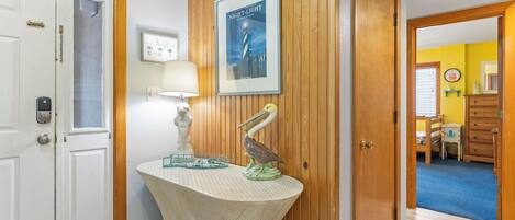 A hallway with a wooden door, a wall-mounted lamp, a framed poster, and a decorative pelican sculpture.