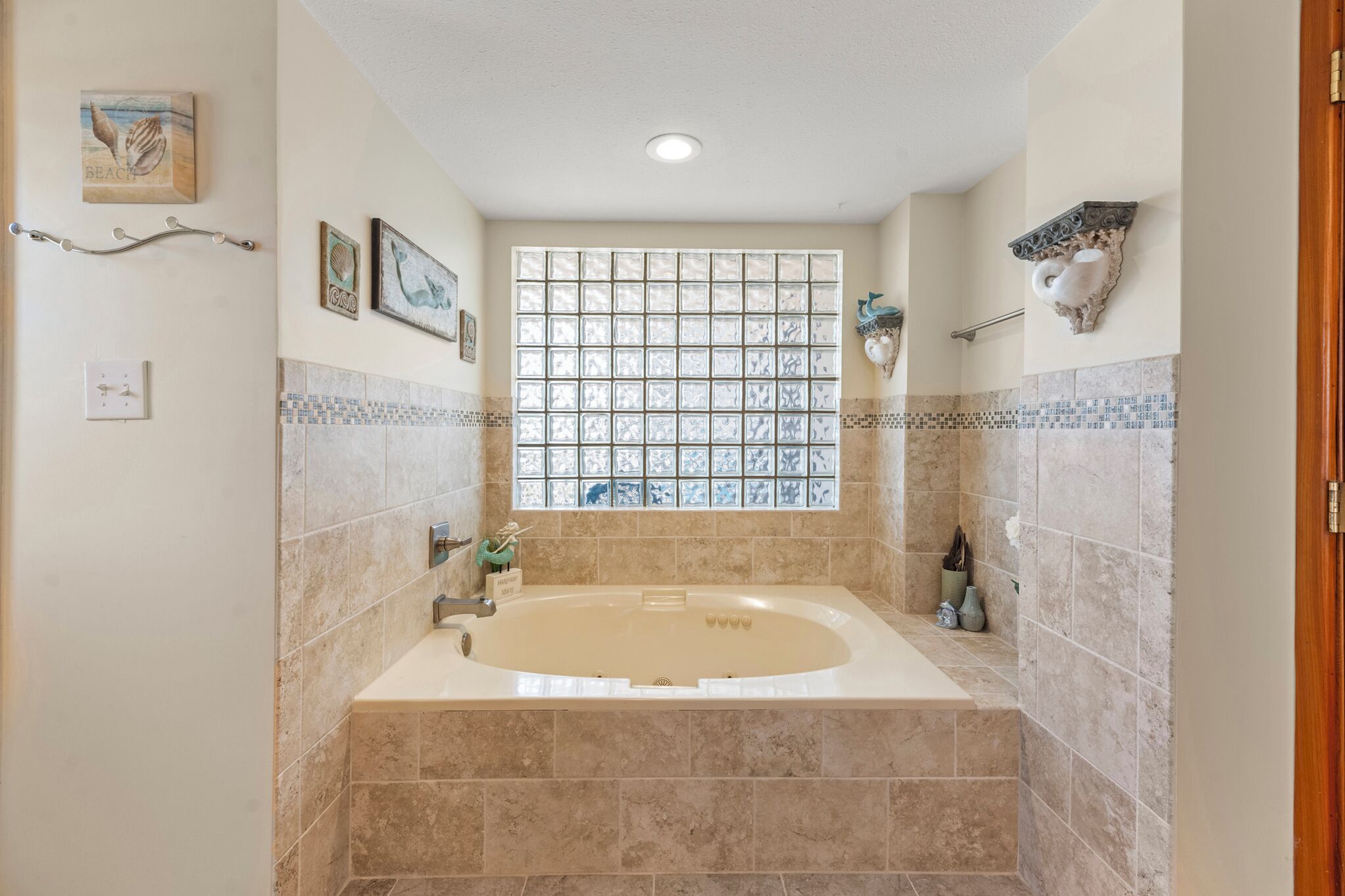 A spacious bathroom with a large bathtub, a window with a grid pattern, and decorative wall art.
