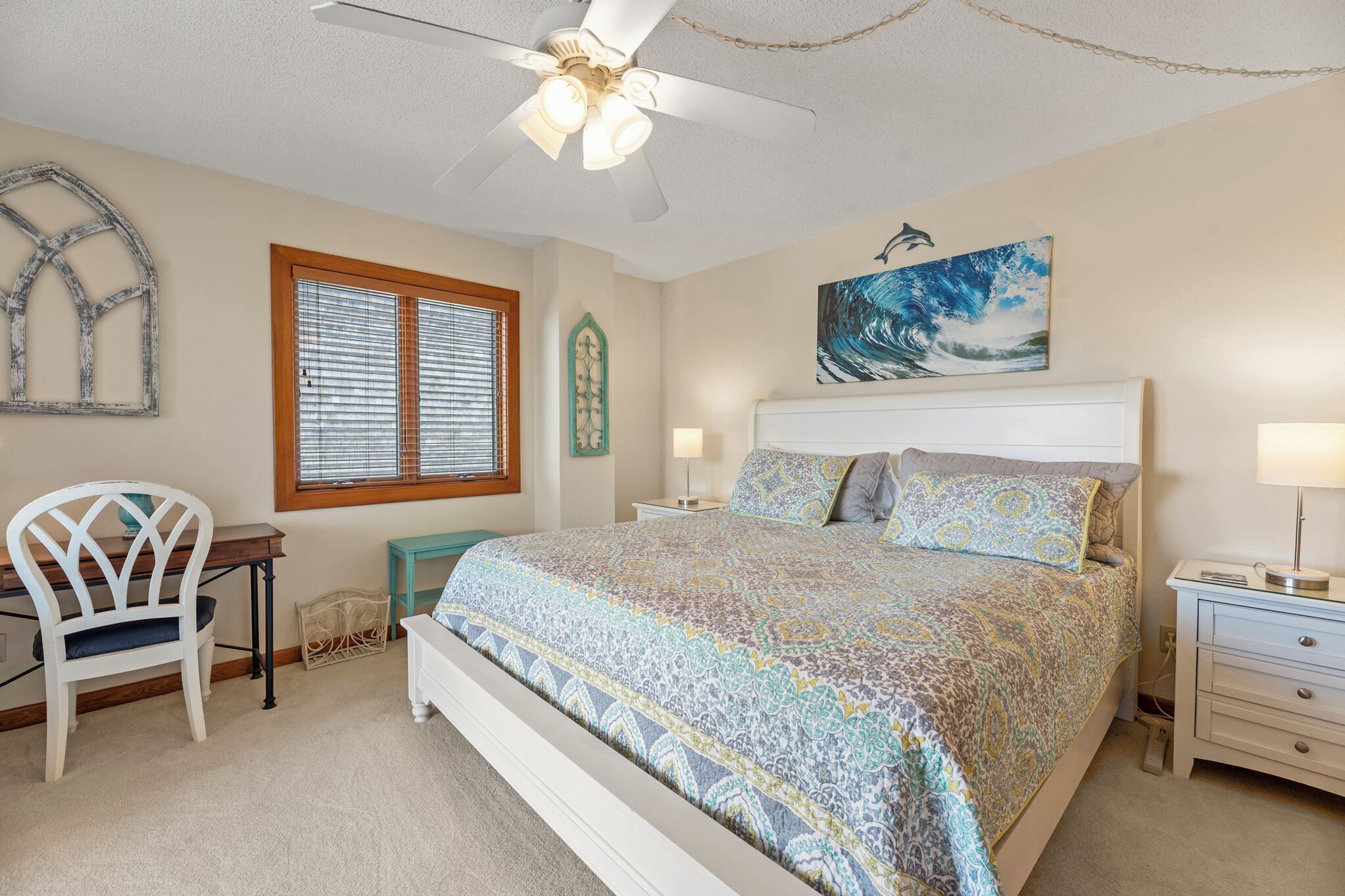 A bedroom with a bed, a desk, a chair, a ceiling fan, and a window with blinds.