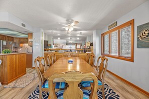 A dining room with a wooden table and chairs, a kitchen in the background, and a ceiling fan.