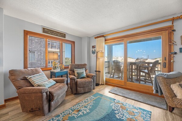 A living room with two brown sofas, a small table, and a large sliding glass door leading to an outdoor patio.