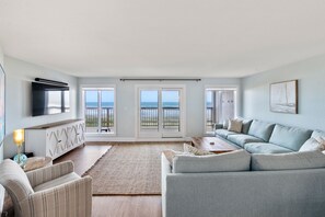 Relax in this stylish living room with a sofa set, entertainment unit, and floor lamp, offering a view of the sea from the sliding glass door.