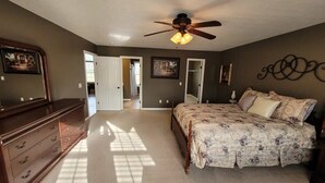 Une chambre à coucher comprenant un lit, une commode, un ventilateur de plafond et des œuvres d’art accrochées aux murs.