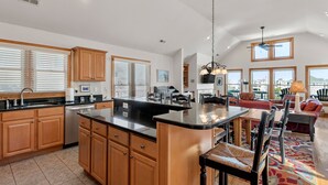 A spacious kitchen with wooden cabinets and a large island, connected to a dining area with a red sofa and chairs. - On Holiday: Oceanside, Private Pool, Spa (Nags Head)