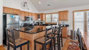A modern kitchen with wooden cabinets, a stainless steel refrigerator, a microwave, and a large island with bar stools. - On Holiday: Oceanside, Private Pool, Spa (Nags Head)