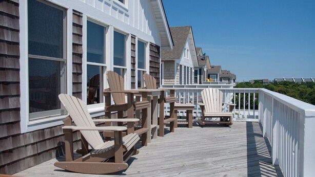 A wooden deck with Adirondack chairs and a table, overlooking a residential area with white houses. - On Holiday: Oceanside, Private Pool, Spa (Nags Head)