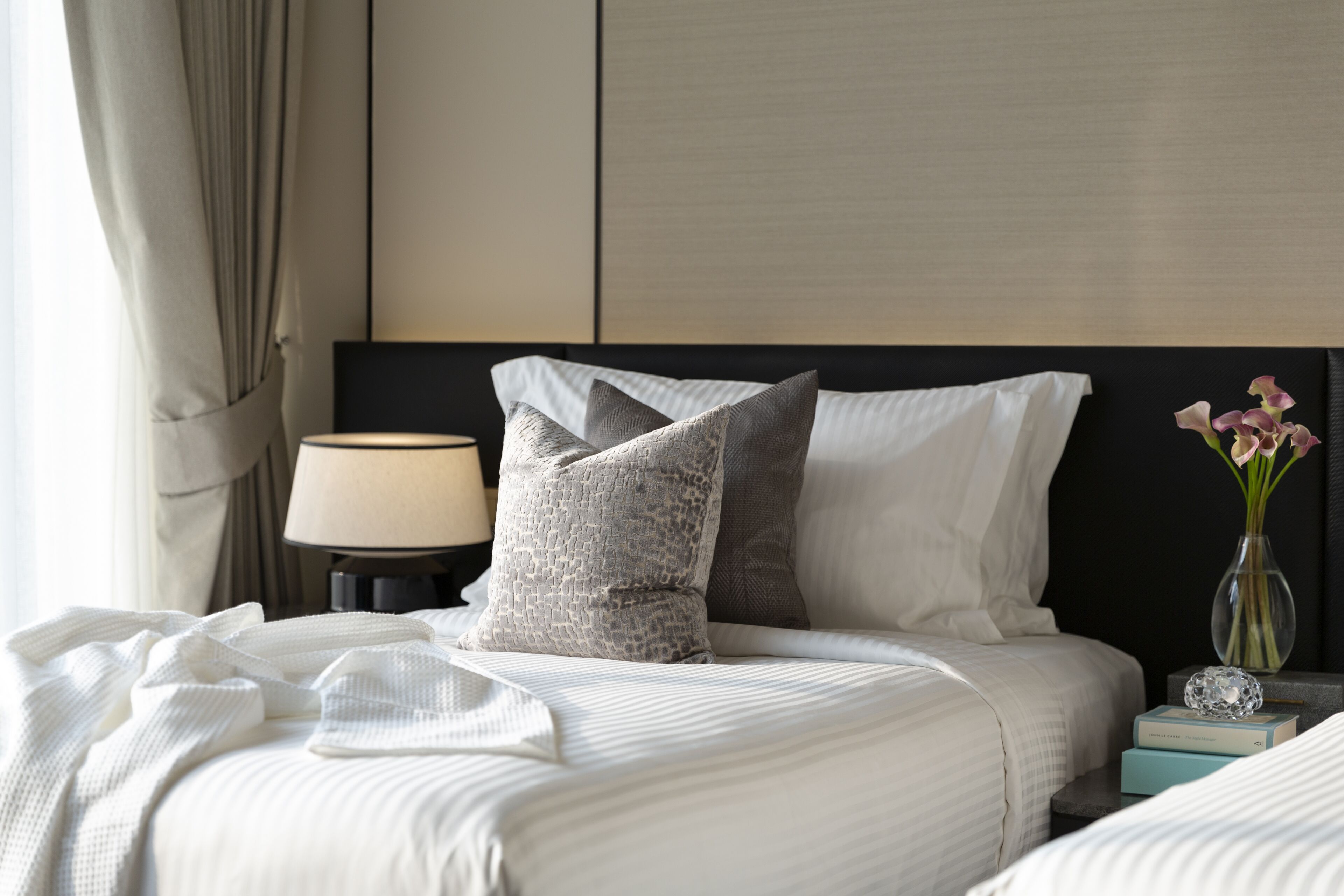 A neatly made bed with white linens, a bedside lamp, and a vase with flowers.
