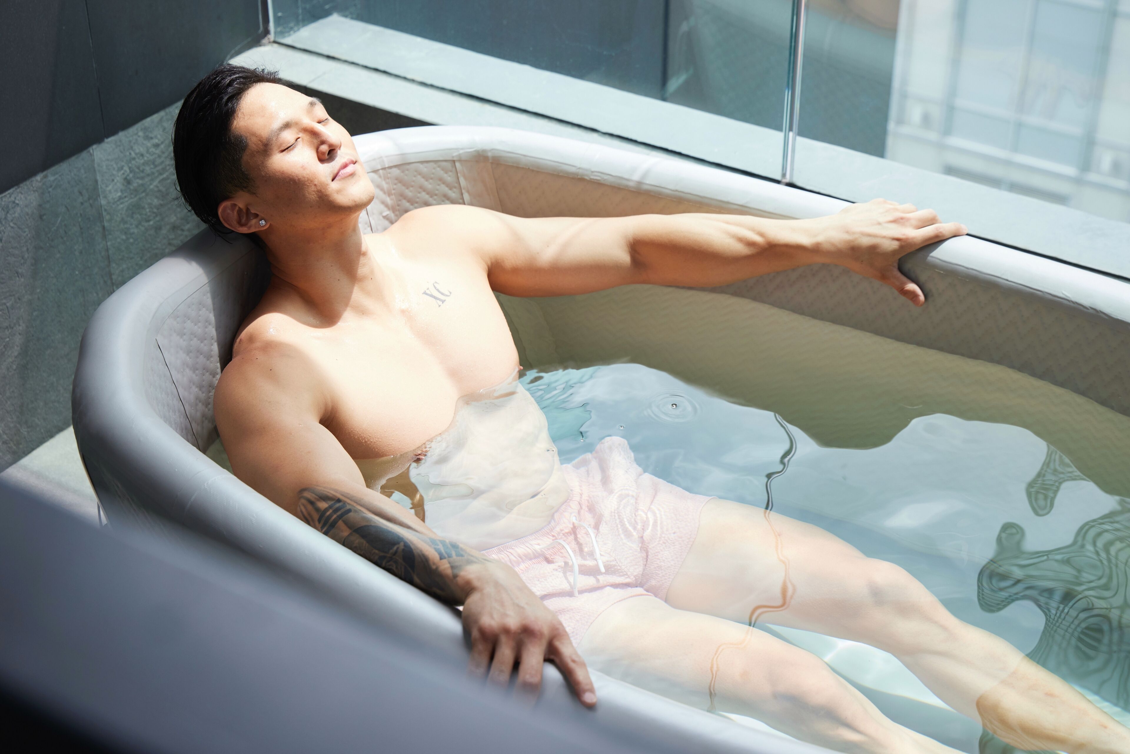A person relaxing in a bathtub with a window in the background.