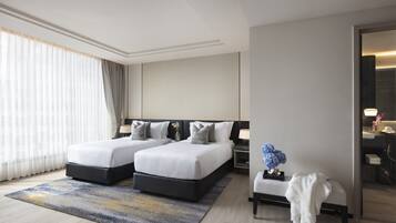 Une chambre d’hôtel moderne avec deux lits, un coin salon et une salle de bain visible à travers une porte ouverte.
