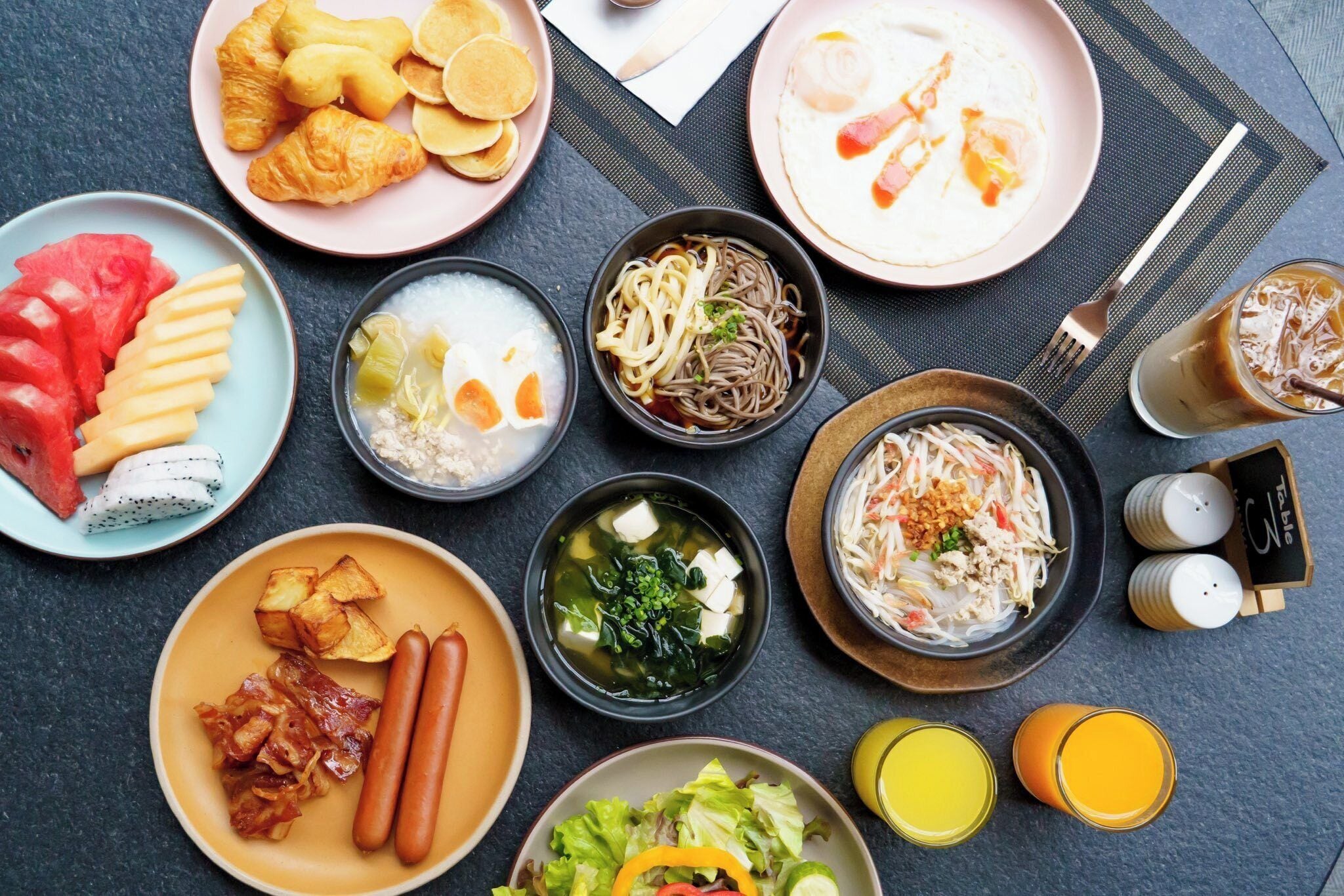 A variety of dishes including noodles, soup, and vegetables, arranged on a table with plates and glasses.