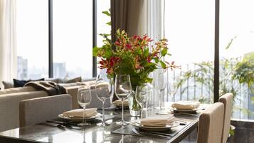 A dining table set with plates, glasses, and a vase of flowers, with a city view in the background.