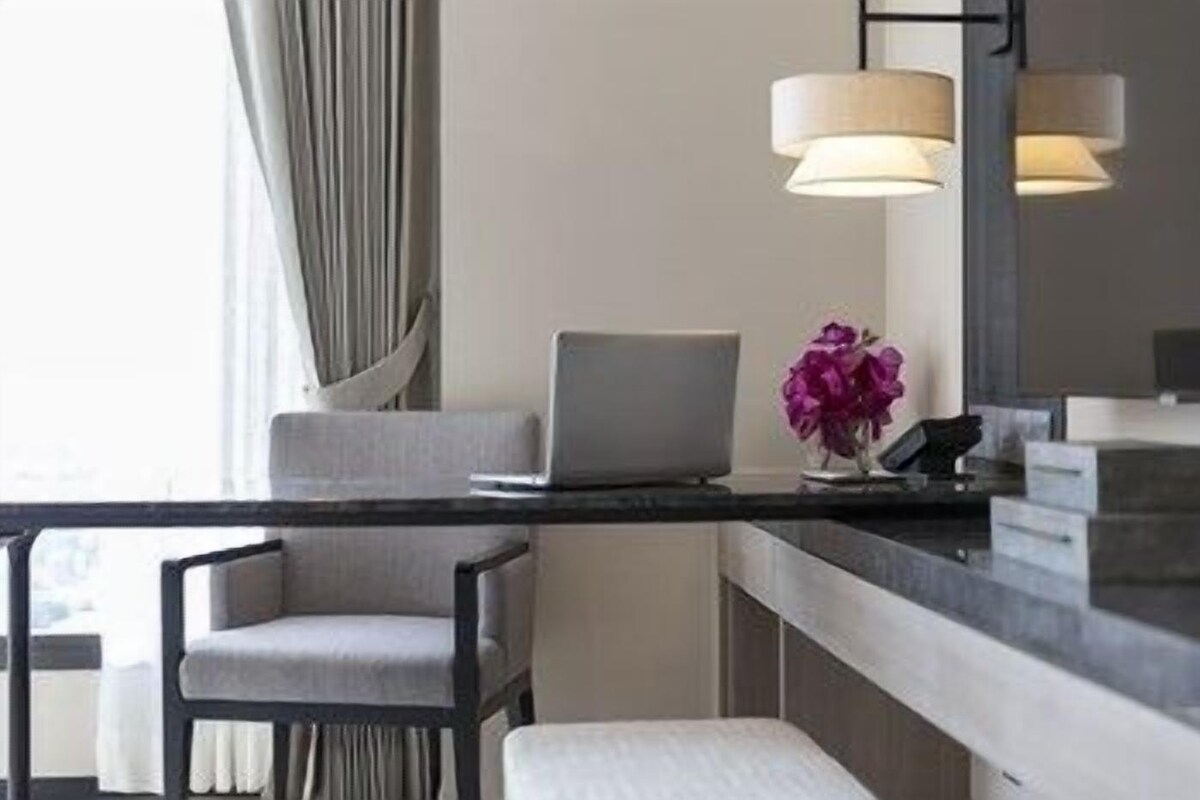 A modern hotel room with a desk, laptop, chair, and a vase with flowers.