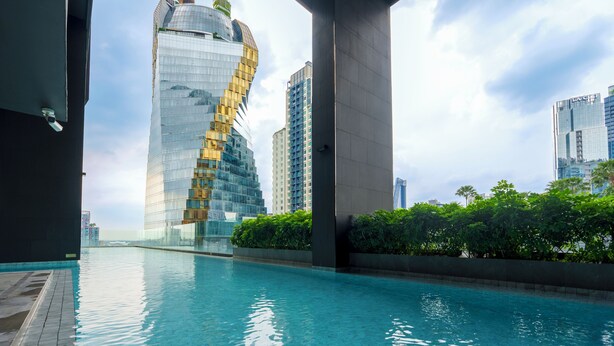 A modern building with a unique spiral design, a swimming pool, and lush greenery in the foreground.