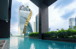 Un edificio moderno con un diseño espiral único, piscina y abundante vegetación en primer plano.