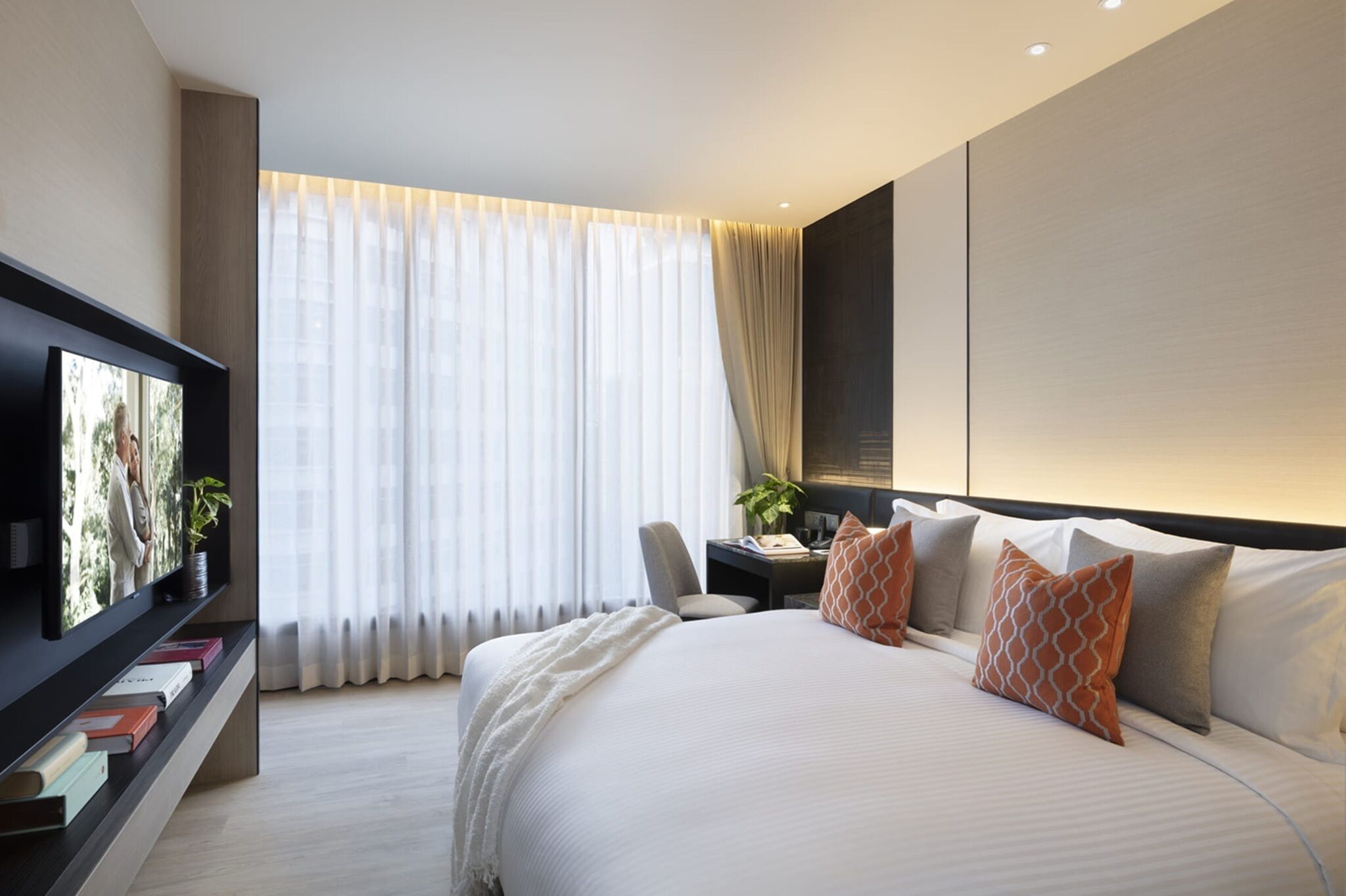 A modern hotel room with a large bed, a desk, a television, and a large window with curtains.