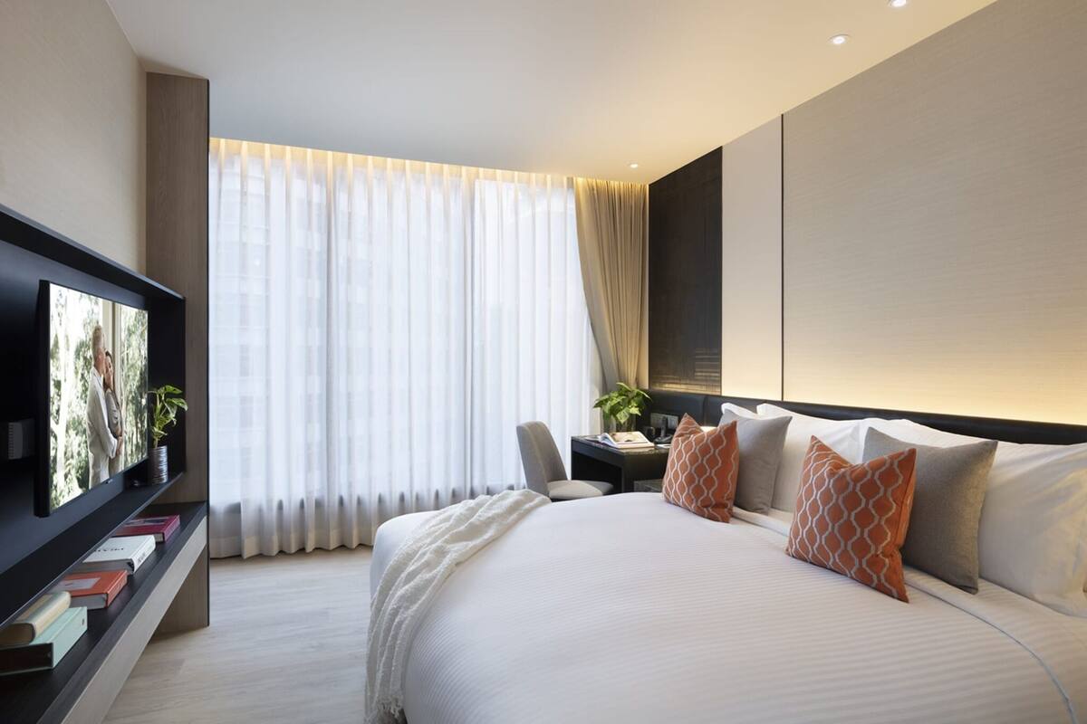 A modern hotel room with a large bed, a desk, a television, and a large window with curtains.