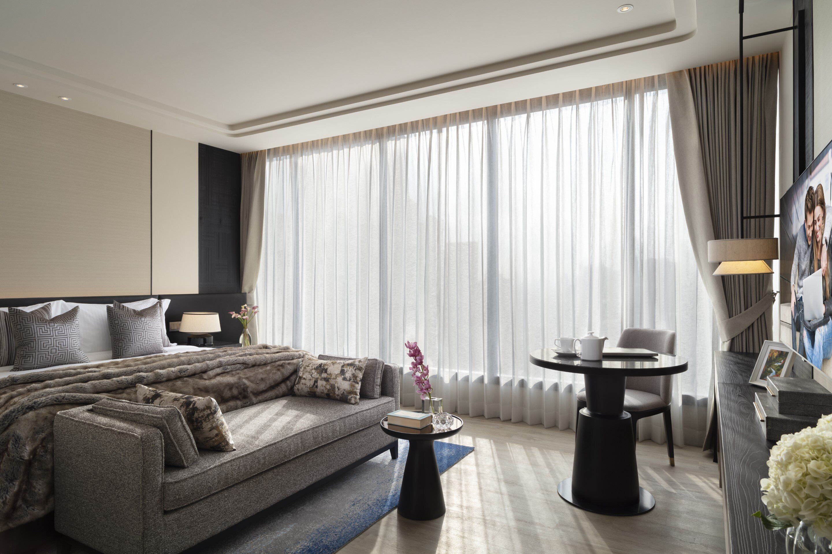 A modern hotel room with a large bed, a sofa, a round table, and a TV.