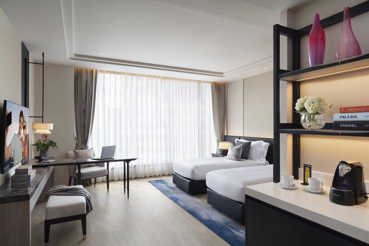 A modern hotel room with a large bed, a desk with a laptop, a television, and a coffee maker.