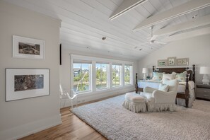 Una camera da letto con una grande finestra, un soffitto in legno e una parete bianca.