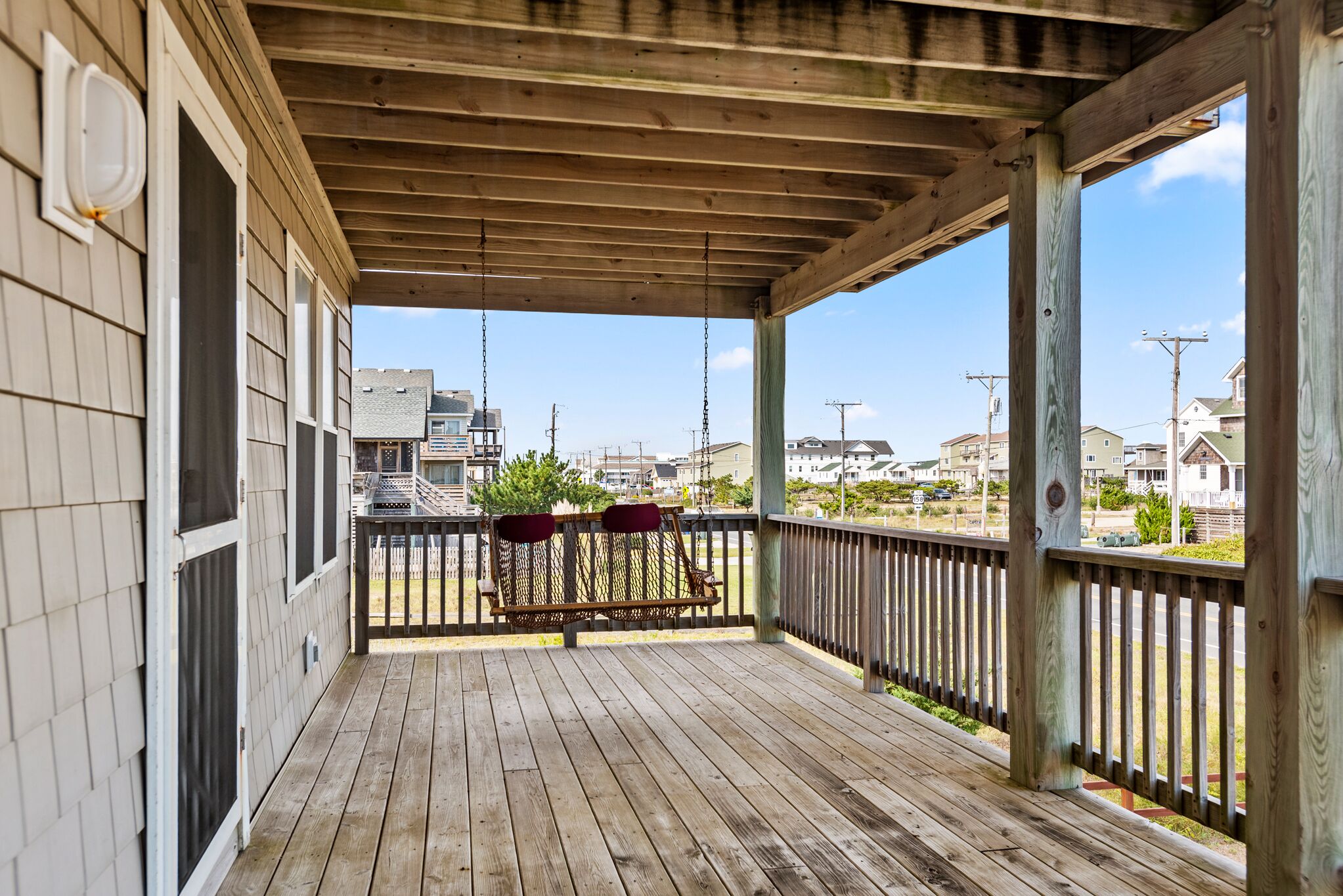 Une véranda en bois avec un banc, une balustrade et une vue sur les maisons au loin.