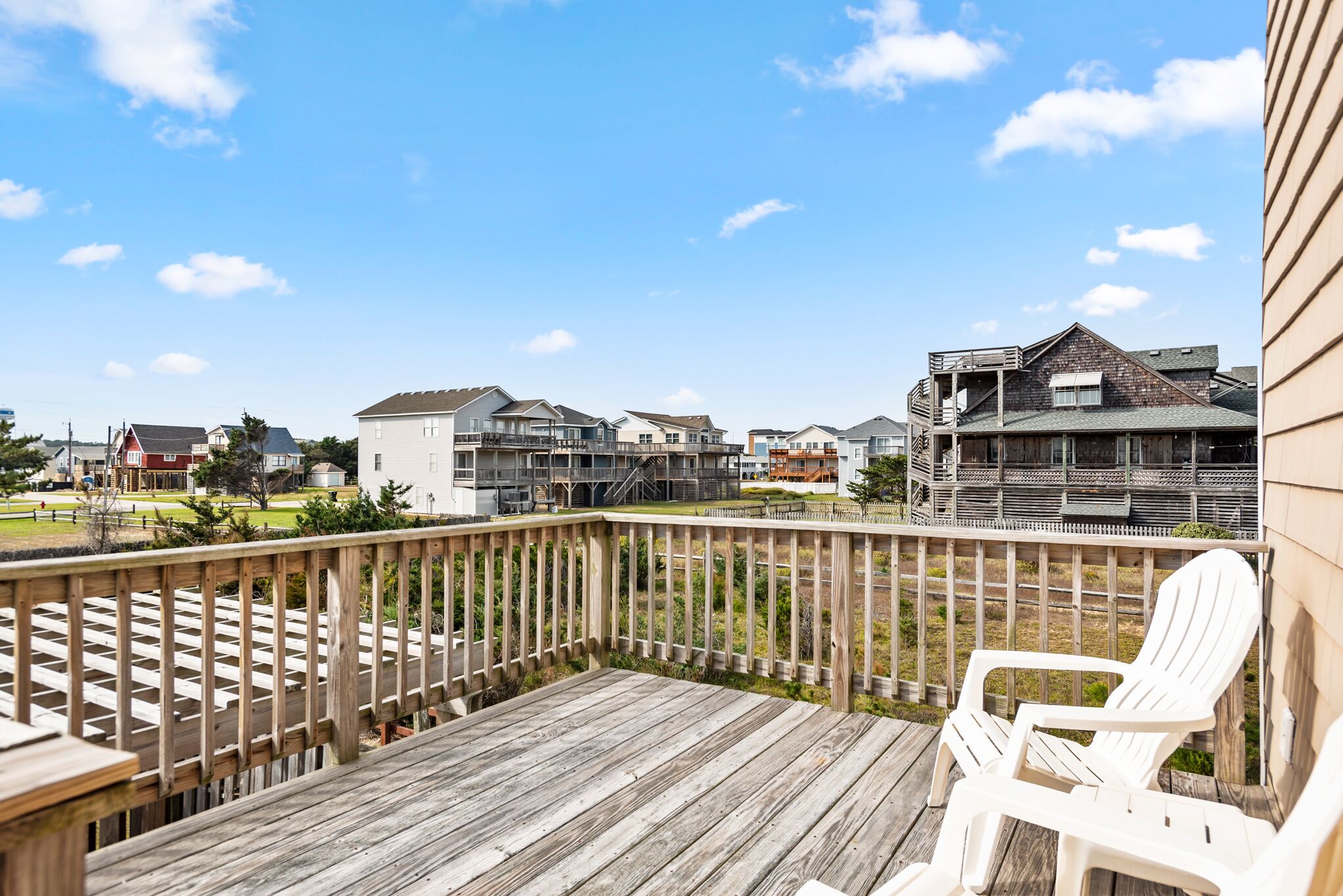 Une terrasse en bois avec une chaise blanche, donnant sur un quartier résidentiel avec des maisons et un ciel dégagé.