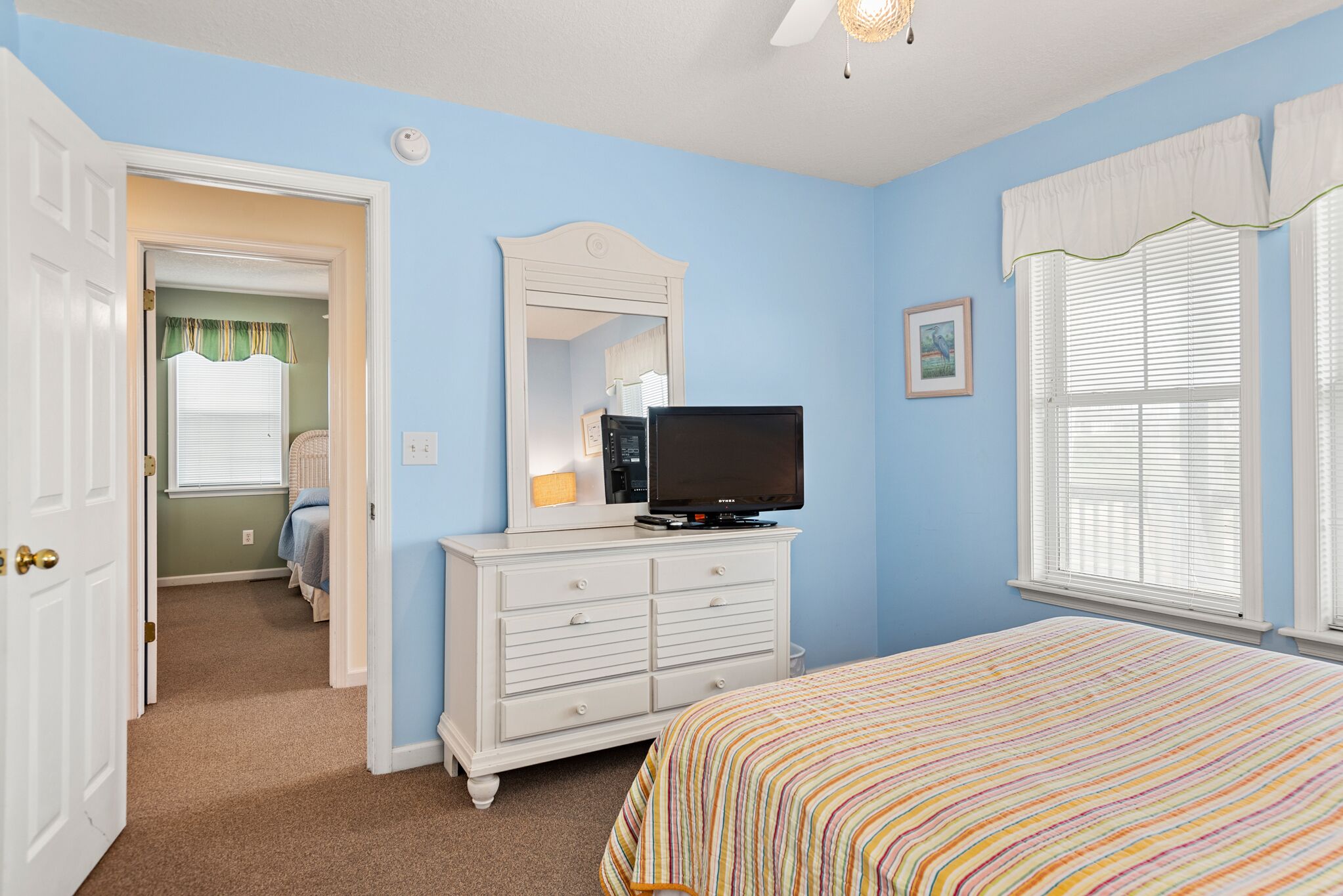 A bedroom with a bed, dresser, television, and a window with blinds.