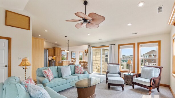 A spacious living room with a light blue sofa, a glass coffee table, and a ceiling fan. - Jockeys Ridge 385: Oceanside, Private Pool, Spa (Nags Head)