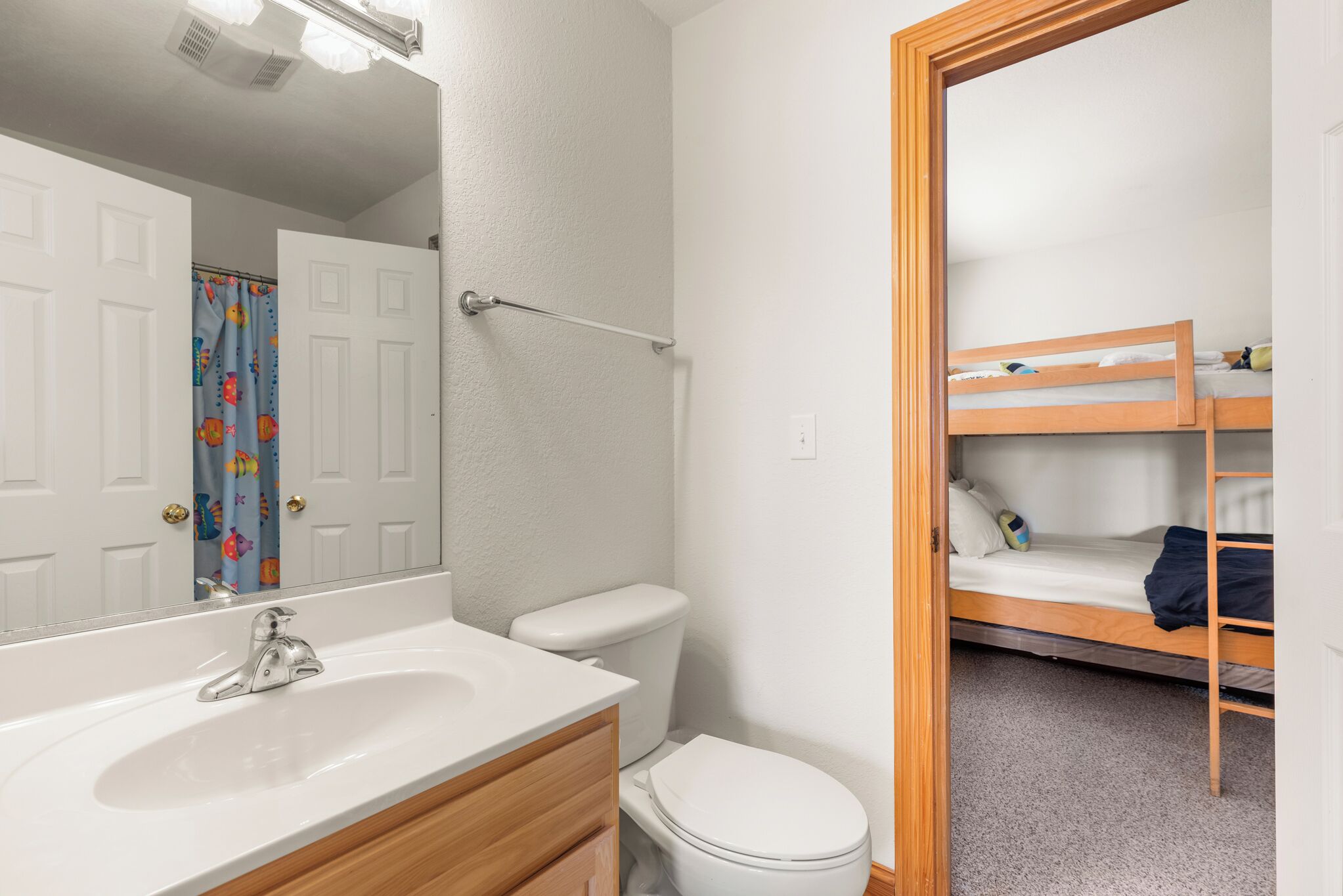 Een badkamer met een wit wastafel, toilet en douchegordijn. Achtergrond toont een stapelbed.