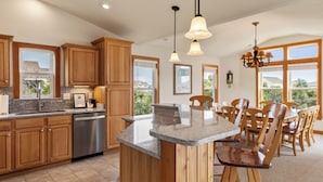 A kitchen with wooden cabinets, granite countertops, stainless steel appliances, and a bar area with bar stools. - Jockeys Ridge 385: Oceanside, Private Pool, Spa (Nags Head)