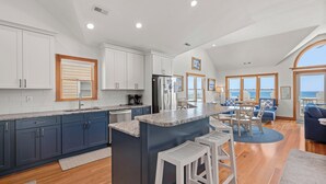 Una cucina moderna con pensili blu scuro, un'isola centrale con sgabelli e vista sull'oceano attraverso ampie finestre.