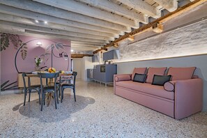 Un salon moderne avec un canapé rose, un coin repas comprenant des chaises et une table, et un espace cuisine doté d’un plan de travail et d’appareils électroménagers.