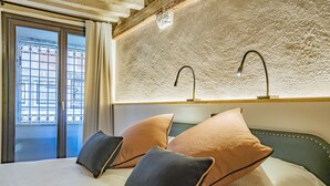 A hotel room with a bed, two pillows, a window with a view, and a textured wall. - Corte Rubbi 5514 Two-bedroom with Canal View (Venice)