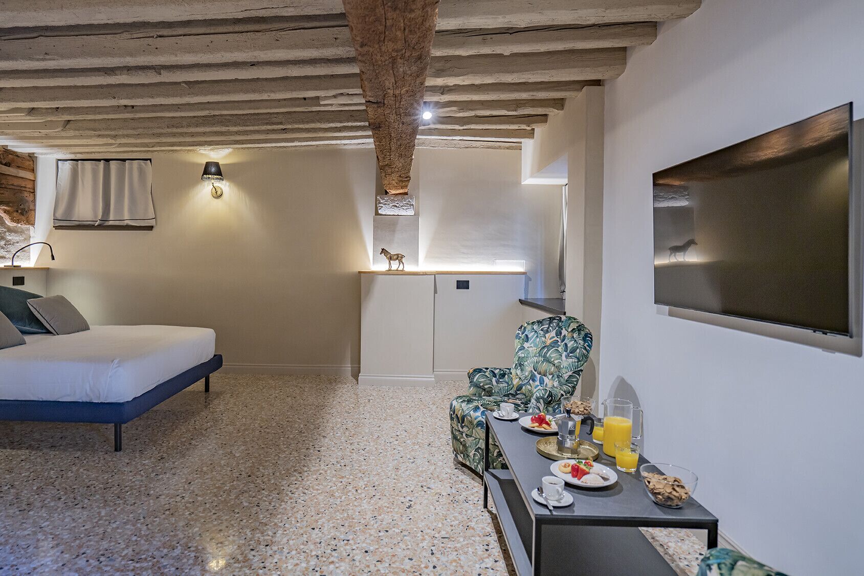 A bedroom with a bed, a chair, a table with breakfast items, and a TV.