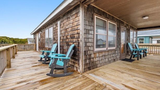 Une terrasse en bois avec des fauteuils à bascule, une véranda et une vue sur une maison dont la façade est recouverte de bardeaux.