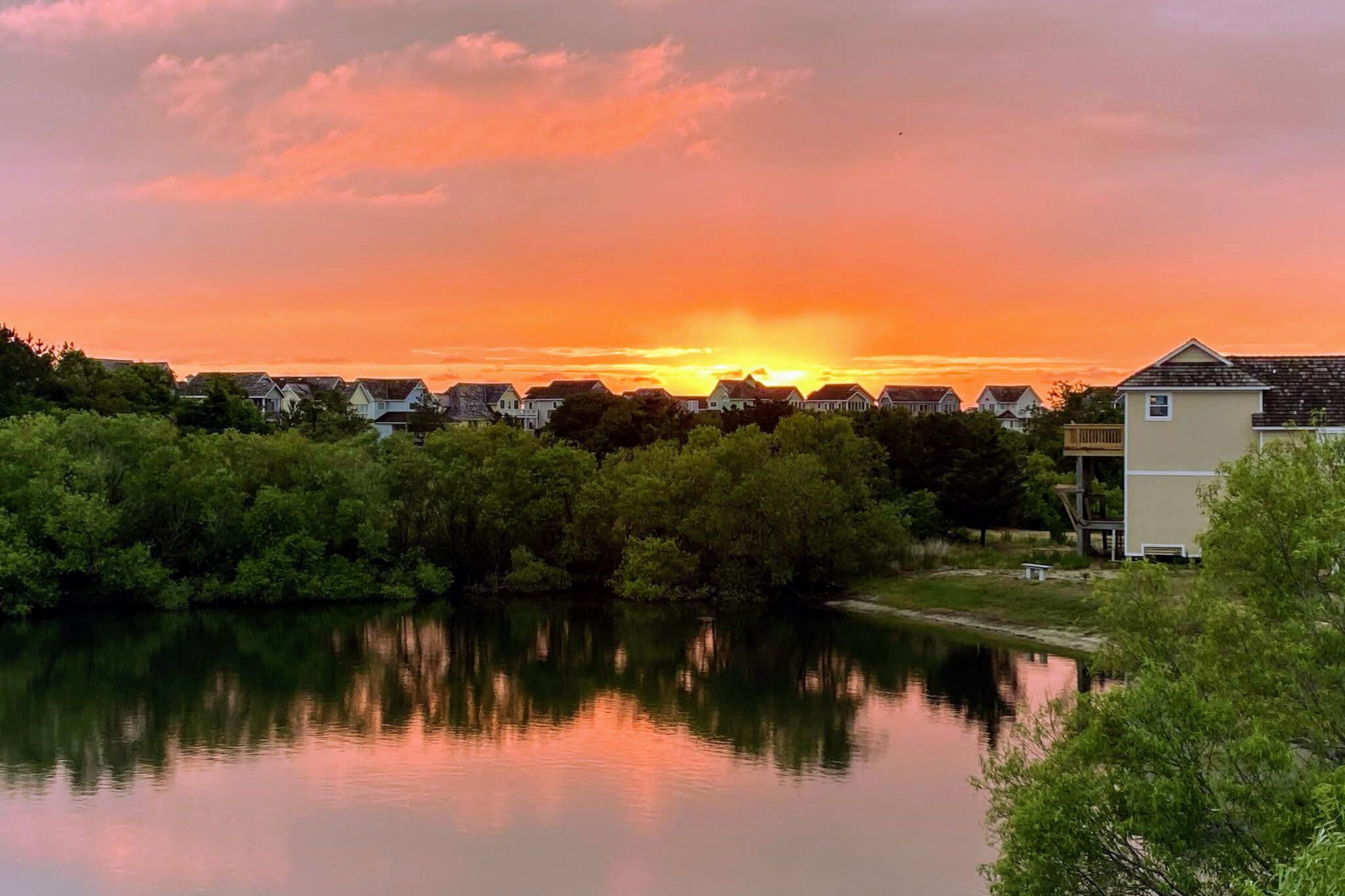A serene lakeside view with houses and trees during sunset.