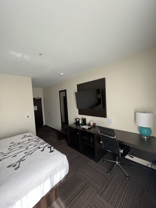 Una habitación de hotel con cama, escritorio, silla, televisor y lámpara.