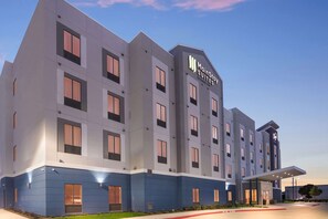 Un moderno edificio de hotel con un llamativo letrero de 'MainStay Suites', varias ventanas y una zona de acceso cubierta.