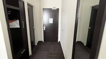 Un couloir étroit au sol recouvert d’une moquette sombre, une porte avec une pancarte et un miroir sur le mur de droite.