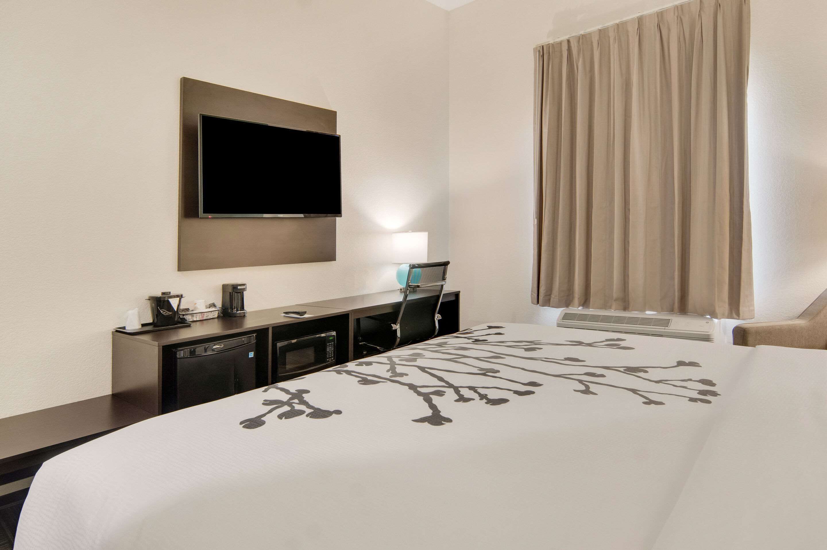 A hotel room with a large bed, a flat-screen TV mounted on the wall, a desk with a lamp, a coffee maker, and a microwave.