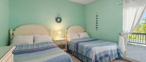 A bedroom with two beds, a ceiling fan, a nightstand with a lamp, a window with curtains, and a wall decoration.